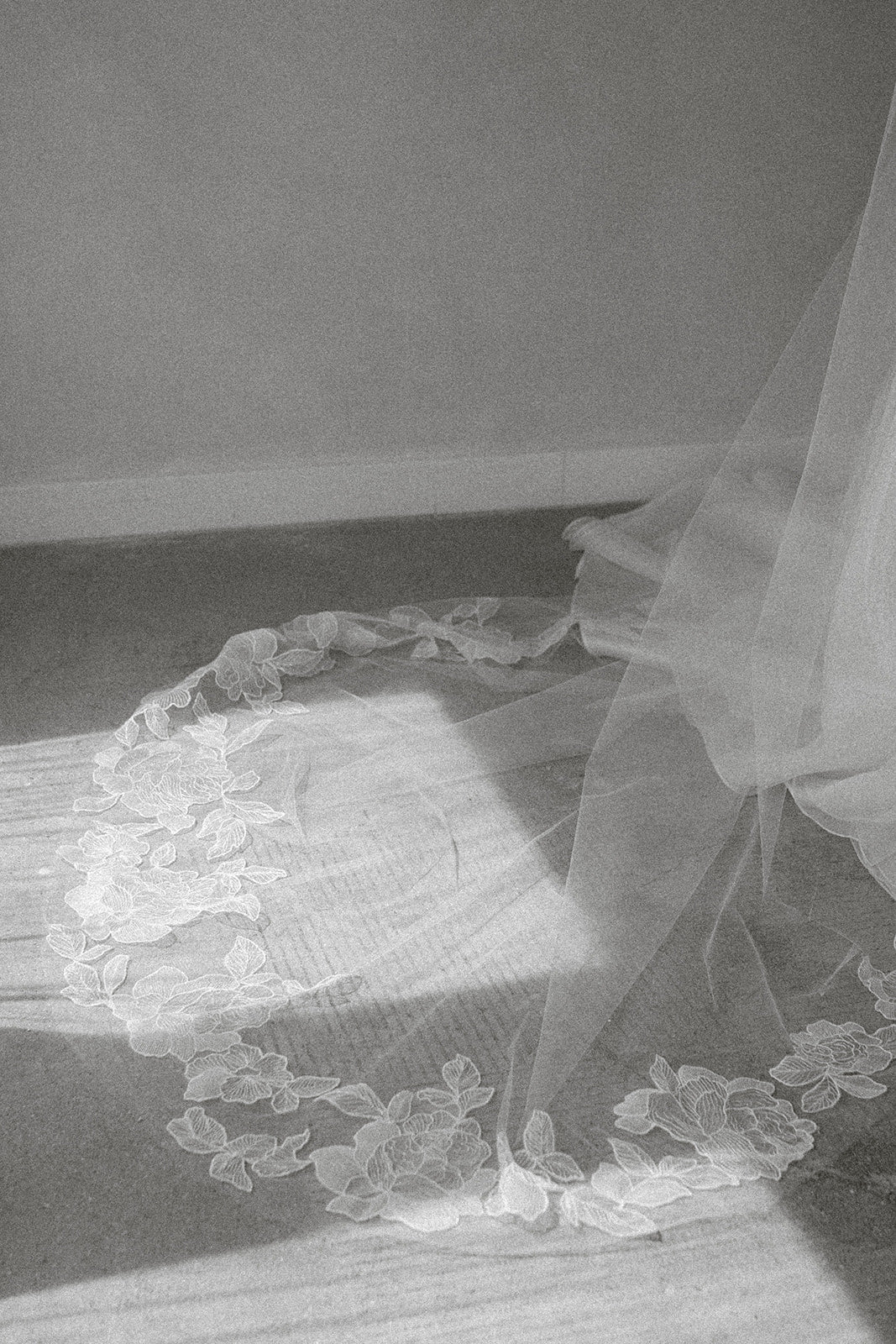 Light ivory peony floral lace wedding veil on a cement floor with a neutral background, shot in black and white.