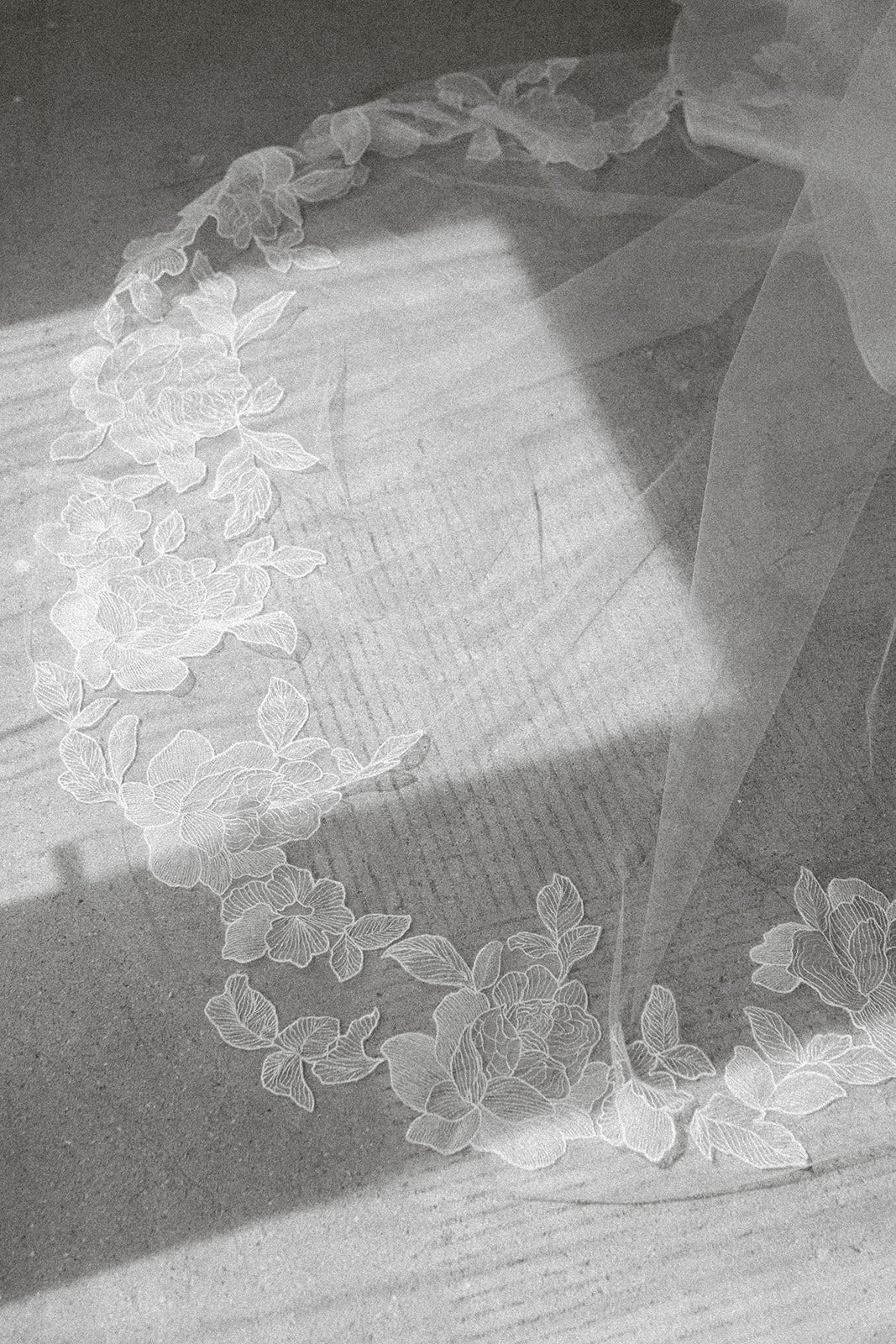 Close-up of a Aunyalune Reverie peony embroidered floral bridal veil on a cement surface.