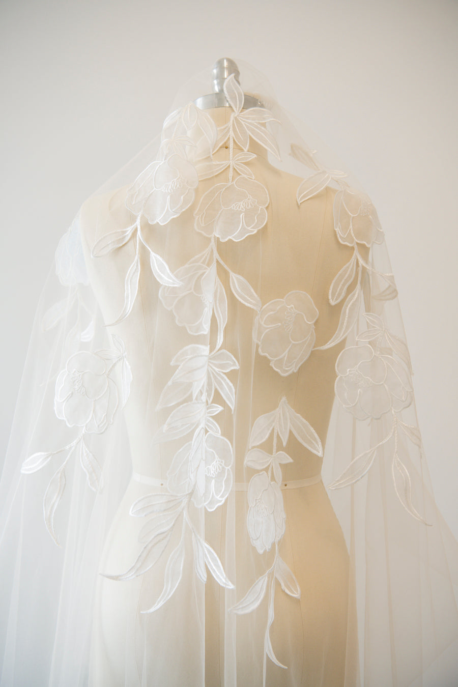 Handcrafted cathedral veil in warm ivory with floral embroidery from crown to fingertip, pictured on a mannequin