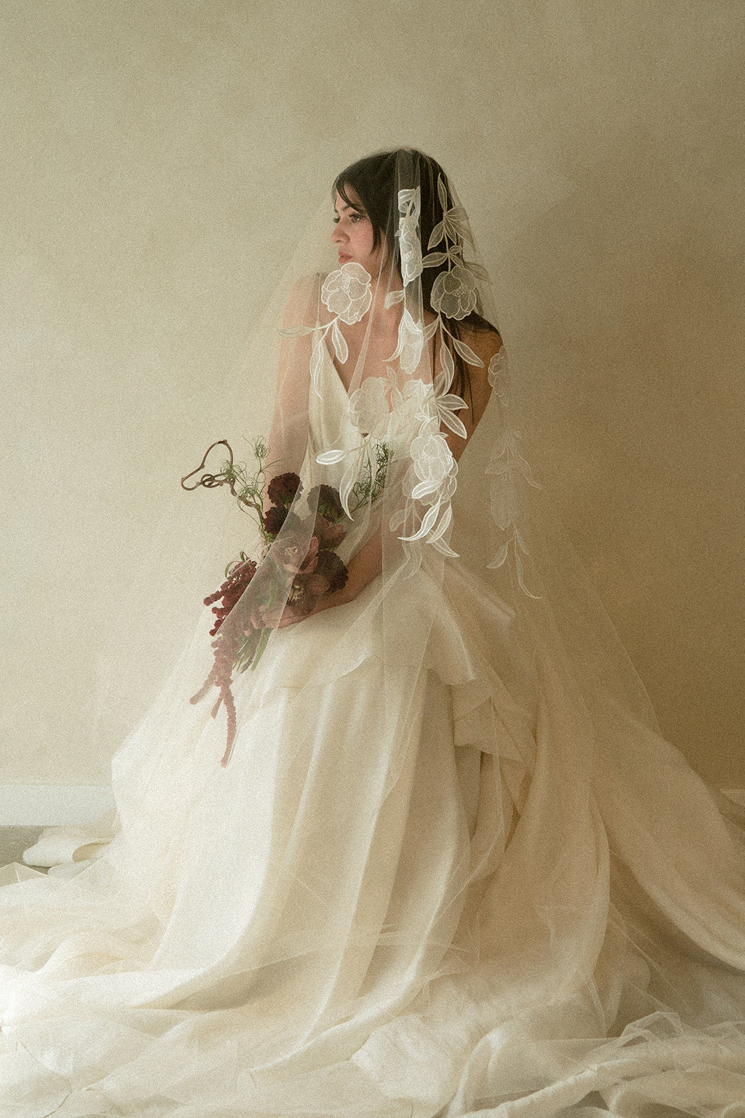 Emotive bride looking into the distance wearing a white dreamy wedding dress and a burgundy bouquet paired withAunyalune Vesper bridal veil 