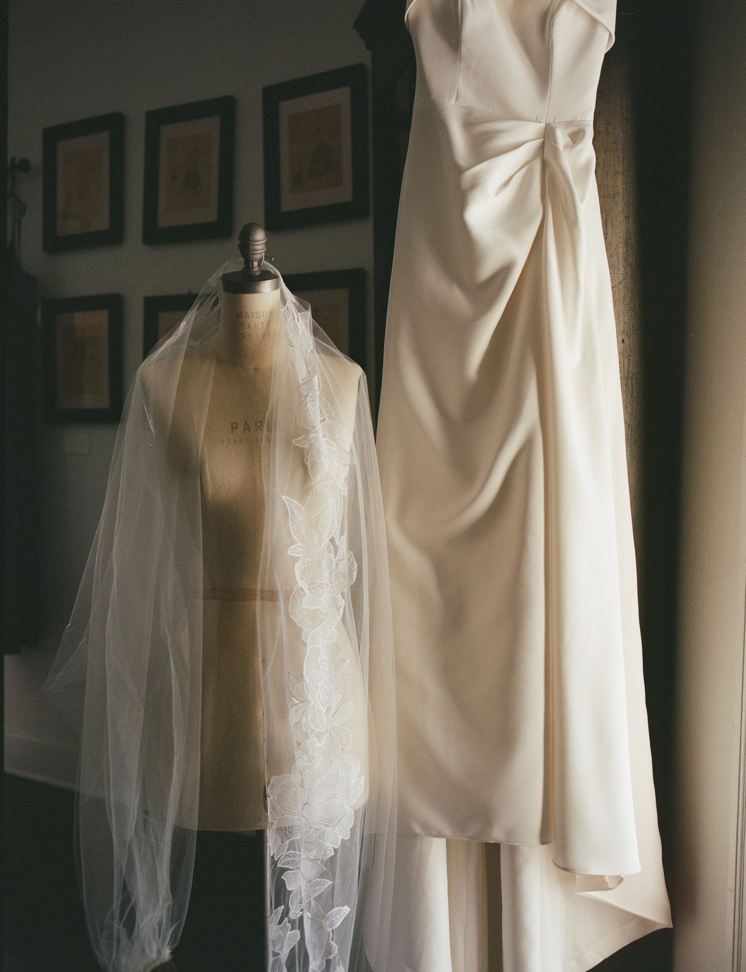 Ivory L'aterlier Fleurish Tiana wedding dress paired with Aunyalune Reverie veil on a mannequin with framed pictures in the background