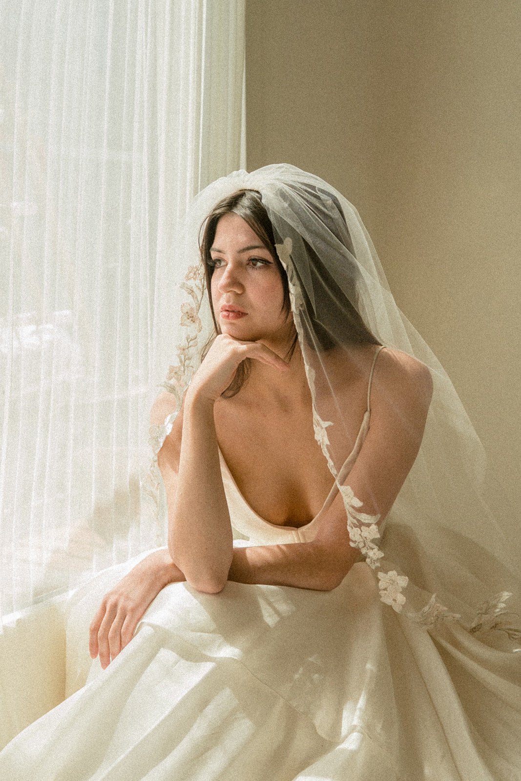 Bride wearing Primevère fingertip veil with embroidered primrose flowers looking out a window